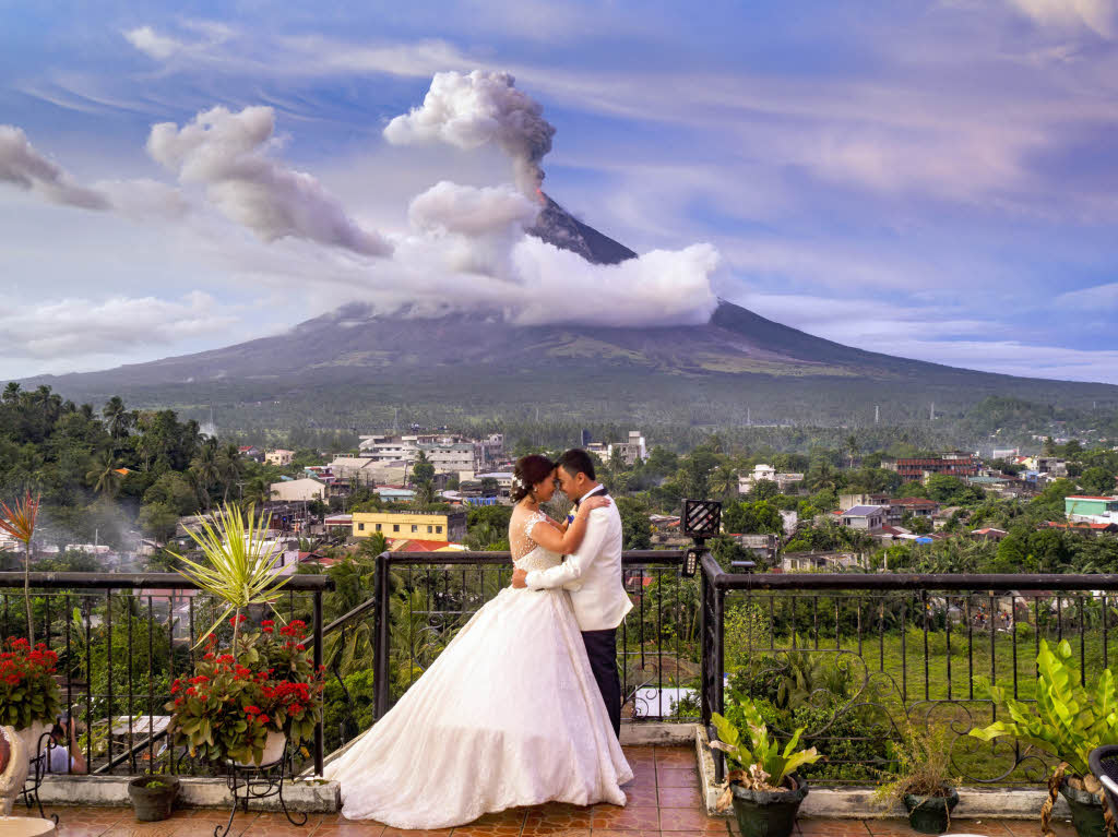Maria Maica de la Cruz und ihr Ehemann, Arlo Gerald de la Cruz, umarmen sich am Donnerstag in Daraga (Philippinen) nach ihrer Hochzeit vor dem aktiven Vulkan Mayon auf der Terasse eines Restaurants.