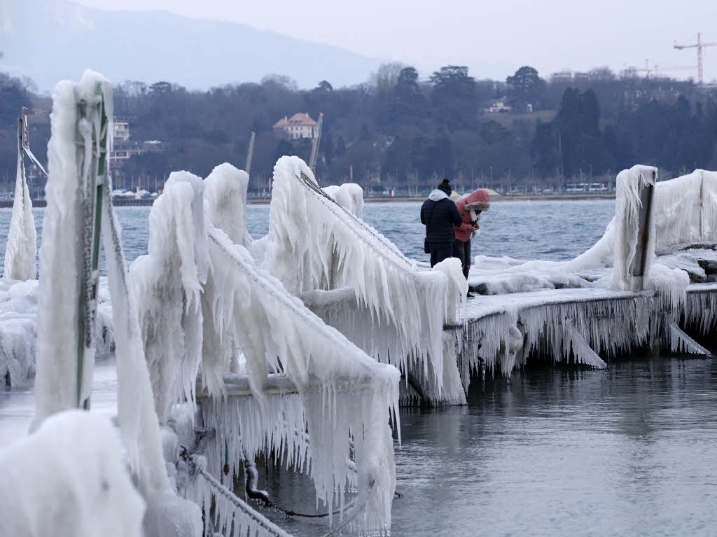 Menschen gehen auf einem Pier am Genfer See entlang, der von Eis bedeckt ist.