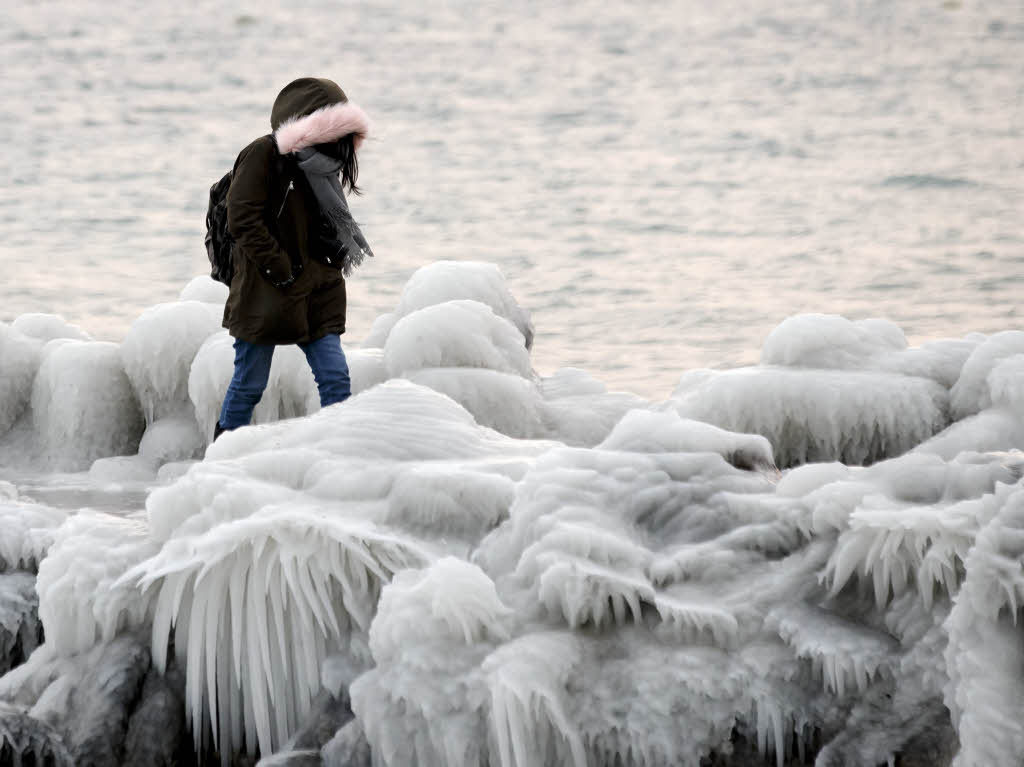 Eine Frau geht auf einem Pier am Genfer See entlang, der von Eis bedeckt ist.