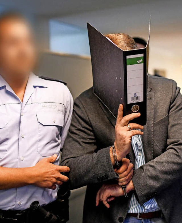 Der Angeklagte Knut S., in Handschelle...ckt sein Gesicht in einem Aktenordner.  | Foto: dpa
