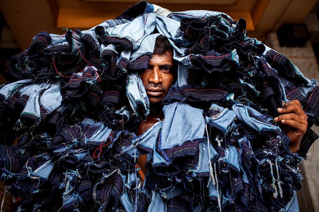 Ein Arbeiter trgt in Dhaka, Bangladesch, Jeanshosen  aus einer Textilfabrik.   | Foto: dpa