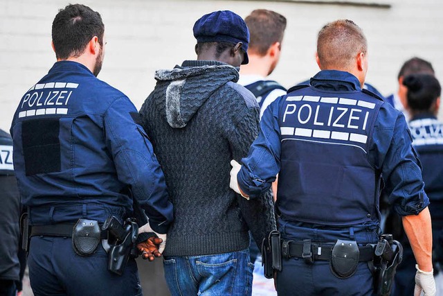 Polizisten fhren bei einer Razzia in ...Flchtlingsheim einen Verdchtigen ab.  | Foto: dpa