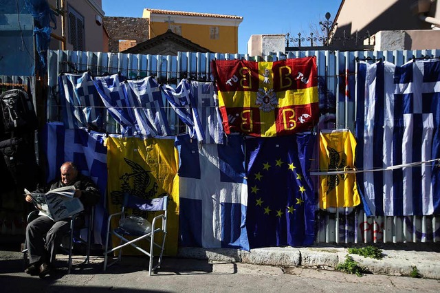 Ein Athener Flaggenverkufer liest Zei...r das hoch verschuldete Griechenland.  | Foto: dpa