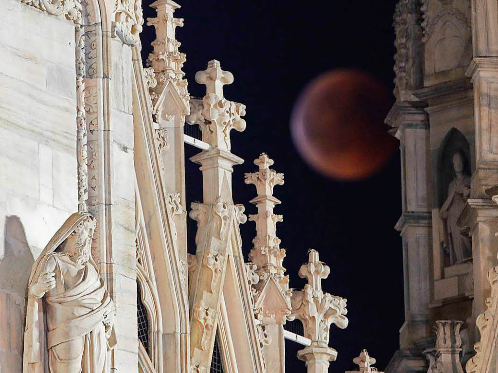 Der rötlich gefärbte Vollmond wird durch die Türme der gotischen Kathedrale des Mailänder Doms gesehen. Der rötlich gefärbte Vollmond wird durch die Türme der gotischen Kathedrale des Mailänder Doms gesehen.