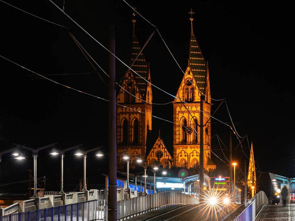 Die Bahnhofsbrücke bei Dunkelheit. Im ... Stühlinger Herz-Jesu-Kirche zu sehen.  | Foto: Michael Guess