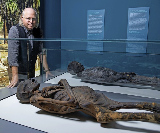 Wilfried Rosendahl, Projektleiter der Ausstellung, mit zwei Mumien im Glaskasten  | Foto: dpa