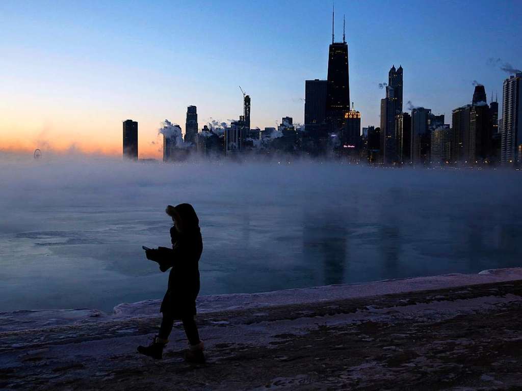 Eine Frau geht vor der Skyline von Chicago am Ufer des Michigansees entlang.