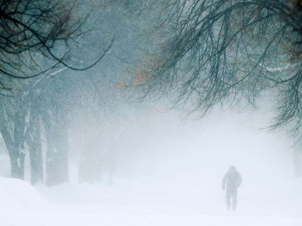 Ein Mann geht whrend eines Schneesturms eine Strae entlang.