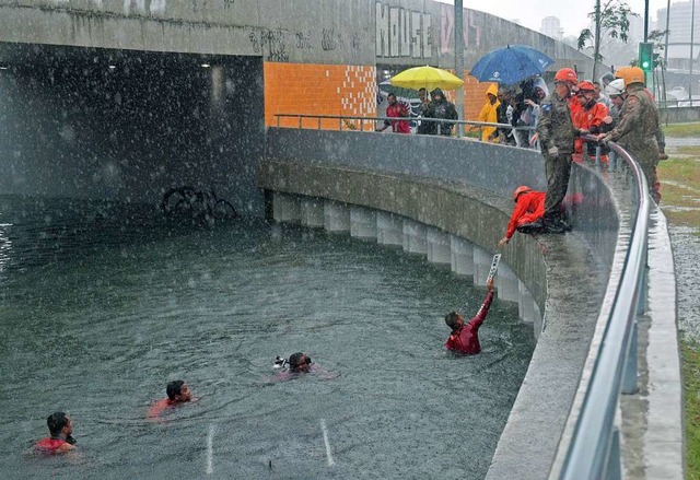 Feuerwehrleute holen das Kennzeichen eines untergegangenen Autos aus dem Wasser.  | Foto: AFP