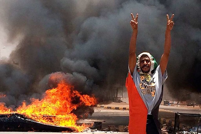 Ein Demonstrant zeigt trotzig das Sieg...hrend im Hintergrund Reifen brennen.   | Foto: Uncredited (dpa)