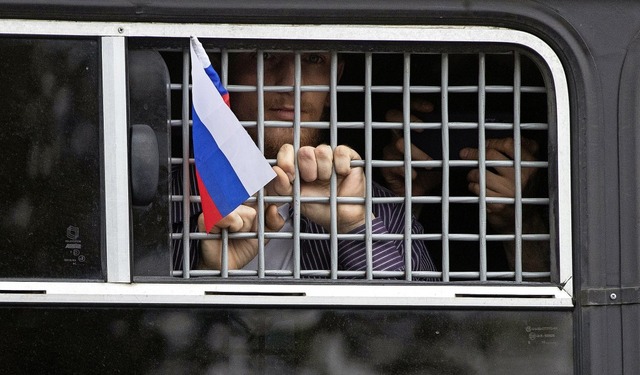Ein verhafteter   Demonstrant schwenkt...izeiauto heraus eine russische Fahne.   | Foto: Pavel Golovkin (dpa)