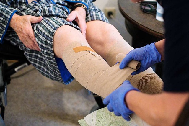 Eine Pflegerin bandagiert die Beine eines Mannes.  | Foto: Jana Bauch (dpa)