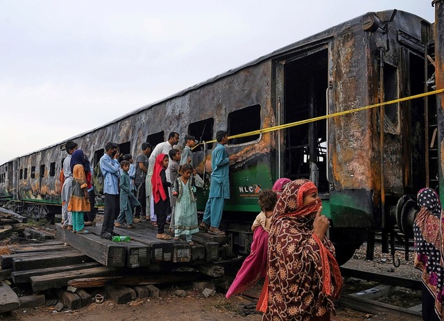 Menschen blicken am Freitag in den ausgebrannten Zug in Pakistan.  | Foto: ARIF ALI (AFP)