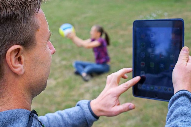 Ein Vater schaut auf sein Tablet, whr...leine mit einem Ball im Garten spielt.  | Foto: Patrick Pleul (dpa)