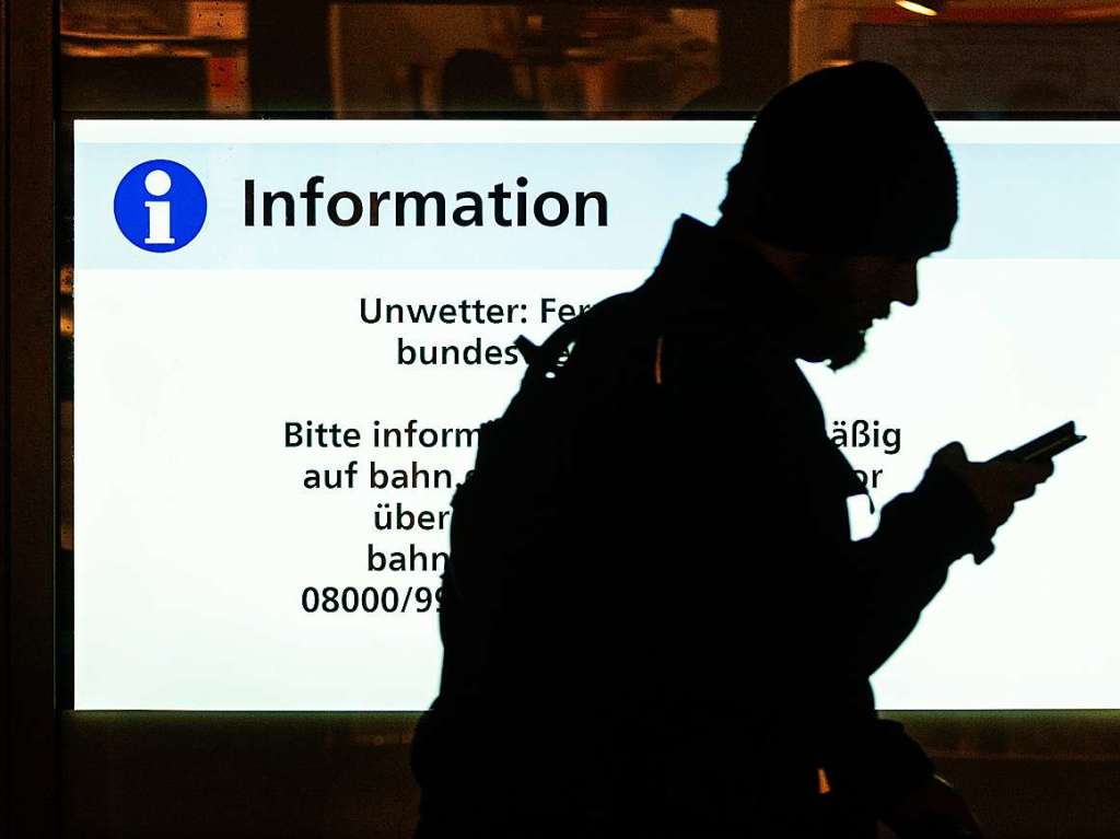 Ein Mann geht mit seinem Smartphone in der Hand an einer Infotafel im Frankfurter Hauptbahnhof vorbei.