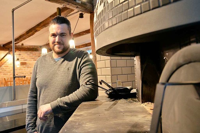 Christian Brombacher vor seinem Holzofen, der mitten im Gastraum steht.  | Foto: Moritz Lehmann