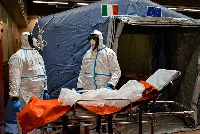 Zwei Mitarbeiter in Schutzanzgen steh...l der Toten und Infizierten weiter an.  | Foto: Diego Puletto (dpa)