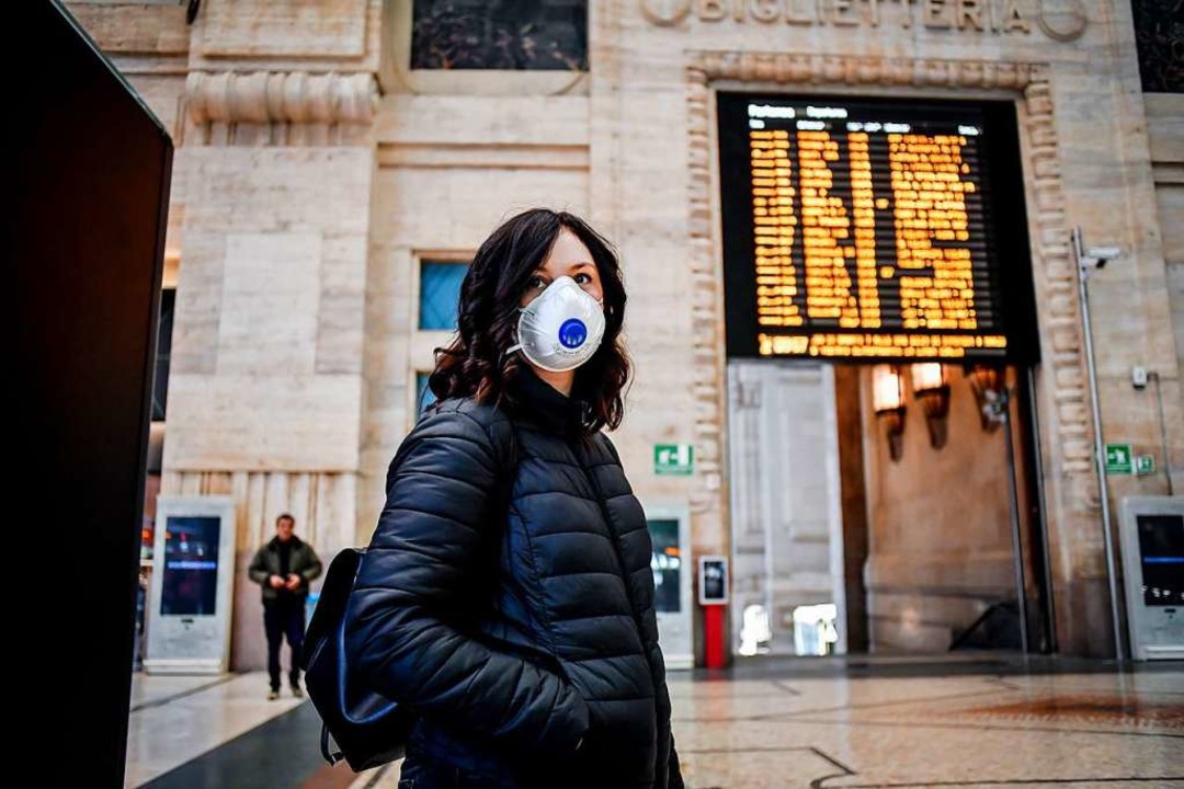 Eine Passantin mit Atemschutz steht im Hauptbahnhof von Mailand.  | Foto: Claudio Furlan (dpa)