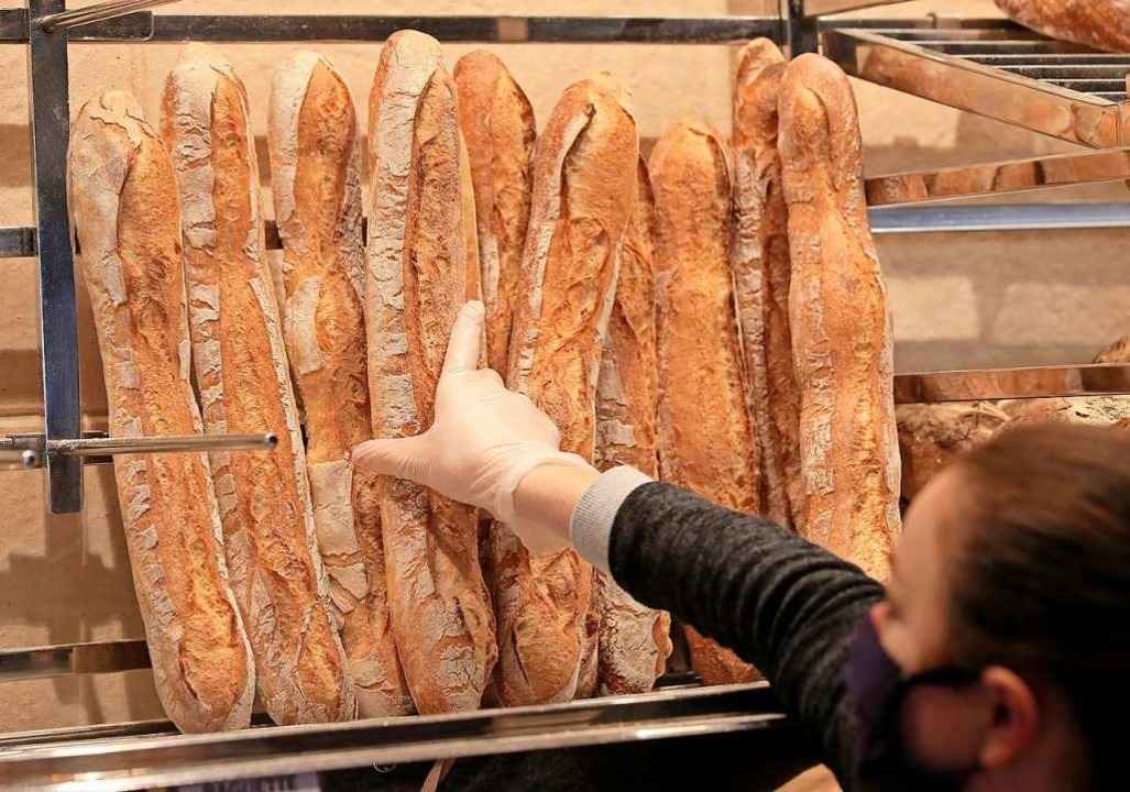 Ein Verk�uferin mit Mundschutz nimmt ein Baguette in einer Pariser B�ckerei.  | Foto: Michel Euler (dpa)