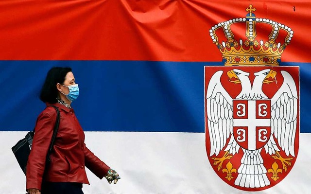 Belgrad: Eine Frau mit einem Mundschut...ationalflagge auf einer Strae vorbei.  | Foto: Darko Vojinovic (dpa)
