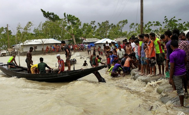 Ein Boot bringt  Menschen im indischen...nd Einheimische einen Damm berprfen.  | Foto: Abu Sufian Jewel (dpa)