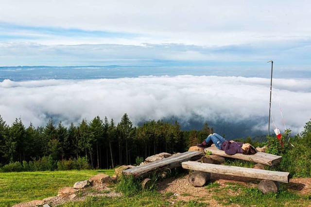 Eine Frau liegt nahe des Gipfel des Ho...heintal unter einer Wolkendecke liegt.  | Foto: Philipp von Ditfurth (dpa)