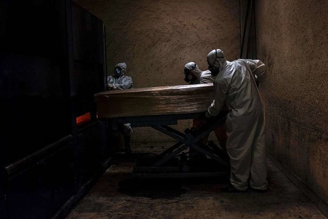 Mitarbeiter eines Krematoriums in Mexi...t tragen in Schutzanzgen  einen Sarg.  | Foto: Jacky Muniello (dpa)
