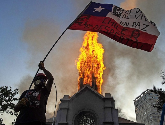 Ein Mann schwenkt vor einer brennenden Kirche die chilenische Flagge.  | Foto: MARTIN BERNETTI (AFP)