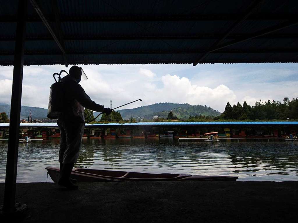 Ein Arbeiter in Schutzkleidung sprht in Indonesien Desinfektionsmittel auf Boote.