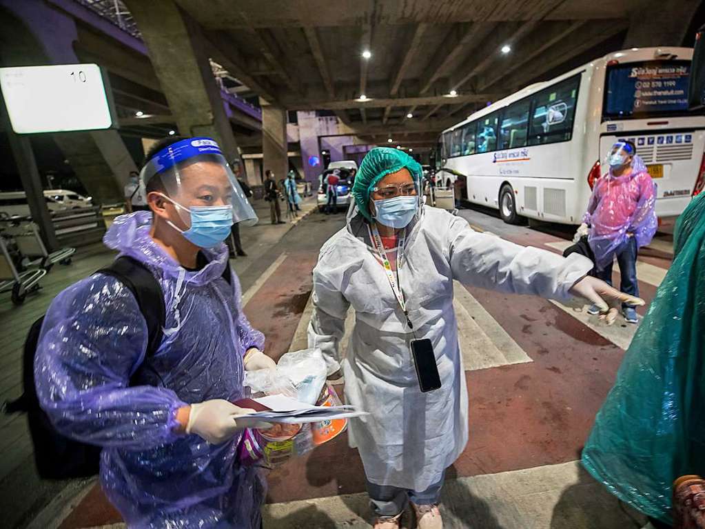 Chinesische Touristen werden am Flughafen in Bangkok von einer Mitarbeiterin des Gesundheitswesens begrt.