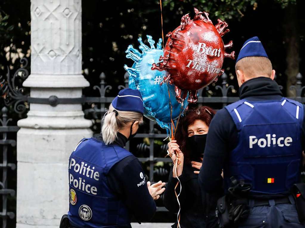 Polizisten in Belgien sprechen mit einer Frau die Luftballons  mit der Aufschrift „Bekmpft das Virus“ hlt.