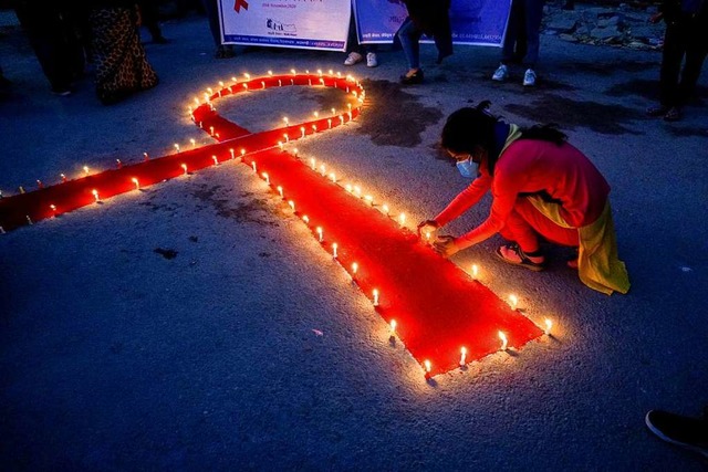 Eine Frau stellt auf einer Veranstaltu...en auf, die eine rote Schleife formen.  | Foto: Sunil Pradhan (dpa)