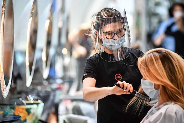 Eine Friseurin bei der Arbeit &#8211; mit Maske und Gesichtsschild (Symbolbild).  | Foto: Claudio Furlan (dpa)