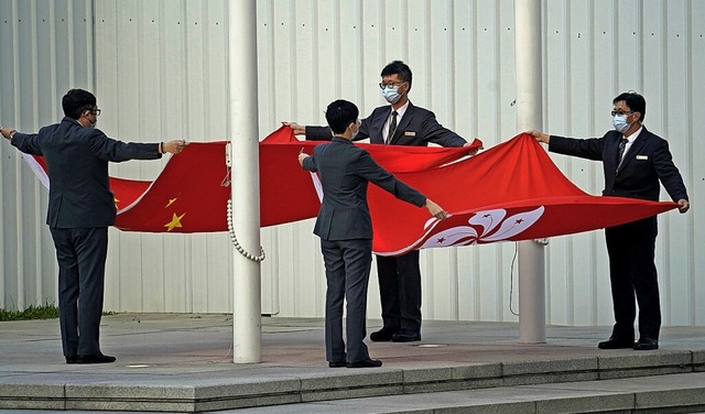 Mitarbeiter falten die chinesische und die Hongkonger Flagge.  | Foto: Kin Cheung (dpa)