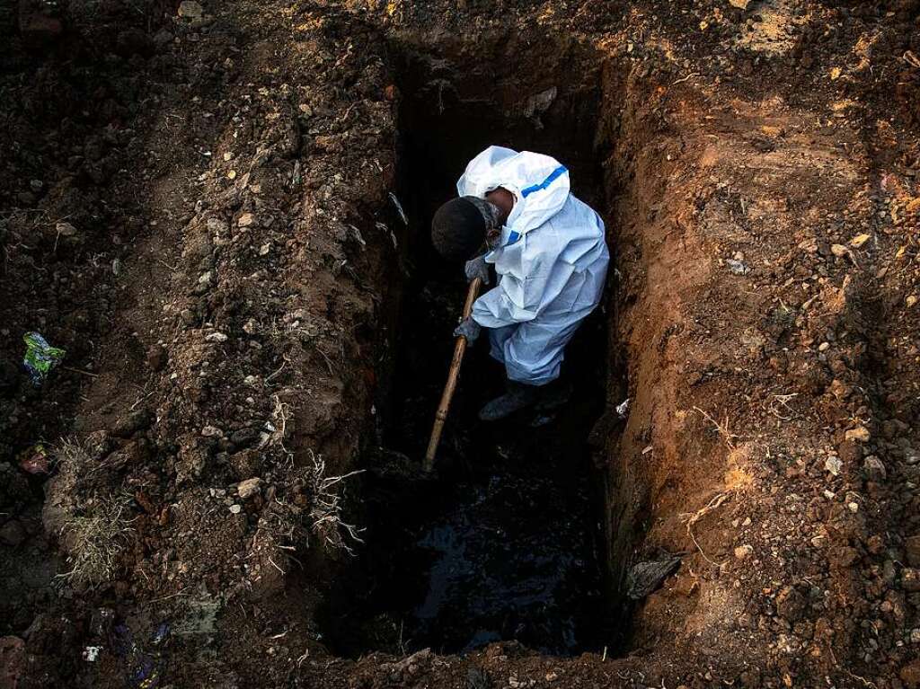 Ein Mann im Schutzanzug hebt Erde aus, um die Leiche einer Person zu begraben, die an Covid-19 gestorben ist.