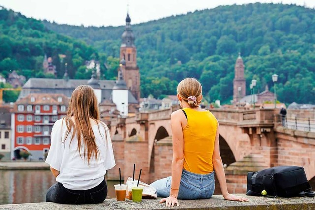 Zwei junge Frauen sitzen in Heidelberg auf einer Mauer (Symbolbild).  | Foto: Uwe Anspach (dpa)