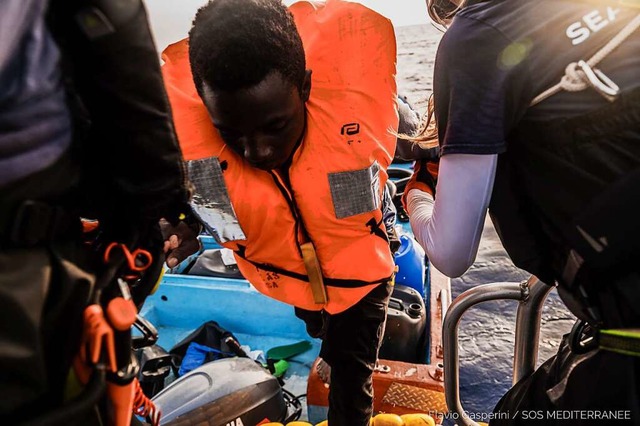Einem Migranten wird aus in einem kleinen Boot in ein Schlauchboot geholfen.  | Foto: Flavio Gasperini (dpa)