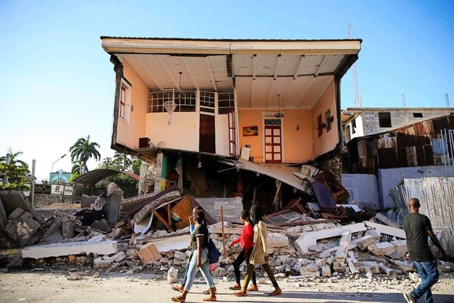 Menschen gehen an einem durch das Bebe...rten Haus in Les Cayes, Haiti, vorbei.  | Foto: Joseph Odelyn (dpa)