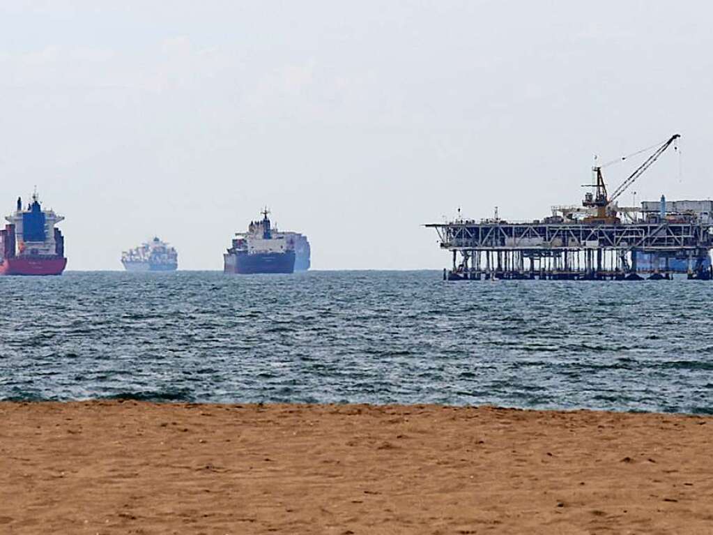 Containerschiffe sind neben einer Bohrplattform im Meer zu sehen.