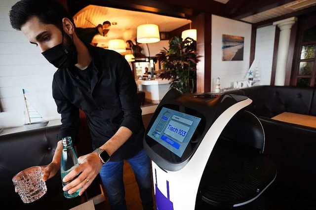 Ein Mitarbeiter serviert im Hafenrestaurant mithilfe des Servierroboters.  | Foto: Marcus Brandt (dpa)