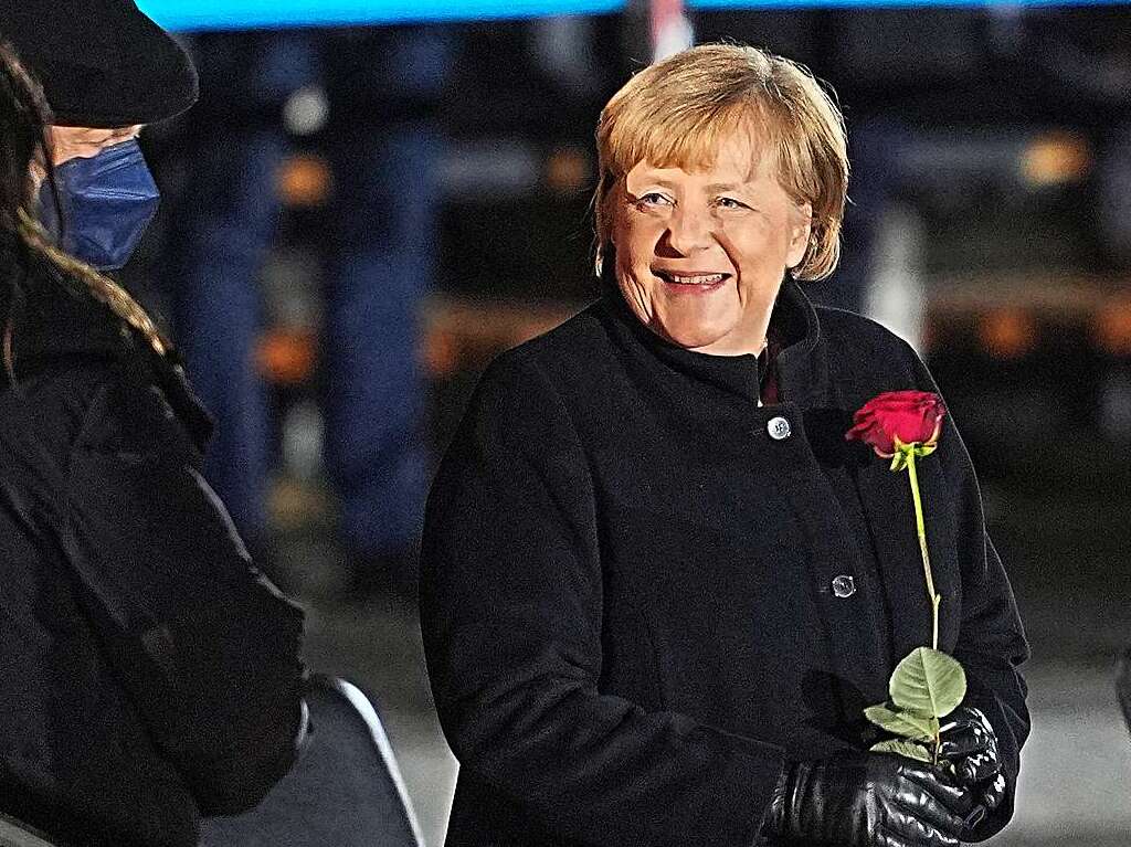 Bundeskanzlerin Angela Merkel (CDU) lacht nach ihrer Verabschiedung durch die Bundeswehr mit einer Rose in der Hand neben ihrem Mann, Joachim Sauer.