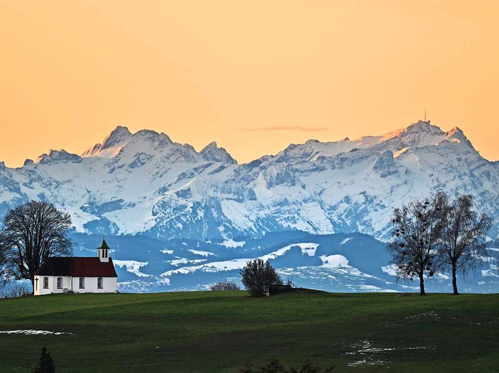 Die Heilig-Kreuz-Kapelle auf dem Kapellenberg bei Amtzell liegt im Morgenlicht. Im Hintergrund sind die Alpen in der Schweiz zu sehen.