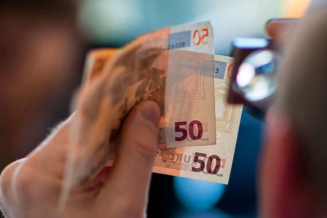Ein Mitarbeiter des Nationalen Analyse...t mit der Lupe zwei 50-Euro-Banknoten.  | Foto: Andreas Arnold (dpa)