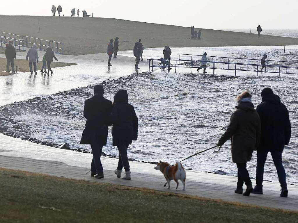 Spaziergnger sind bei Sturm an der aufgepeitschten Nordsee unterwegs.