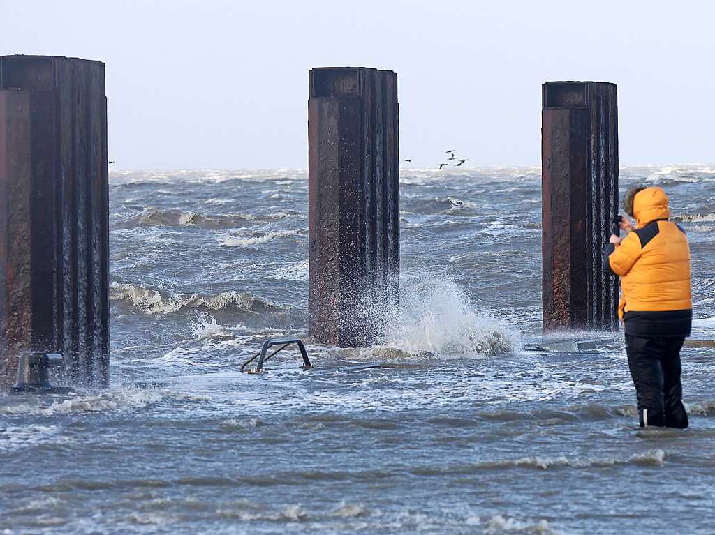 Ein Passant beobachtet, wie das Wasser der aufgepeitschten Nordsee bei Sturm den Fhranleger Dagebll berflutet.