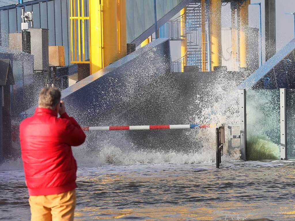 Ein Passant beobachtet, wie die Gischt der aufgepeitschten Nordsee bei Sturm den Fhranleger Dagebll berflutet.