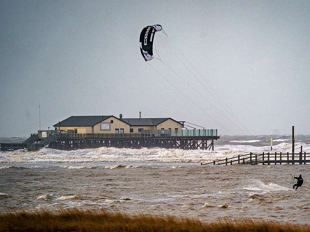 Ein Kitesurfer zieht in dem vom Wind aufgepeitschten Meer seine Bahnen.