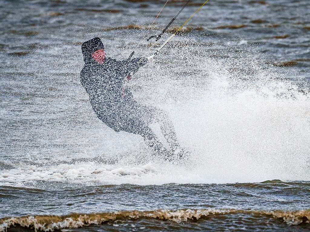 Ein Kitesurfer zieht in dem vom Wind aufgepeitschten Meer seine Bahnen.