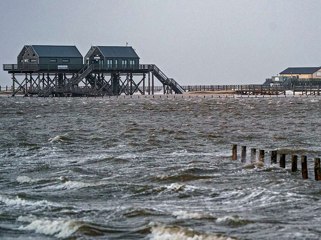 Wellen brechen an den Pfahlbauten am vollstndig bersplten Strand.