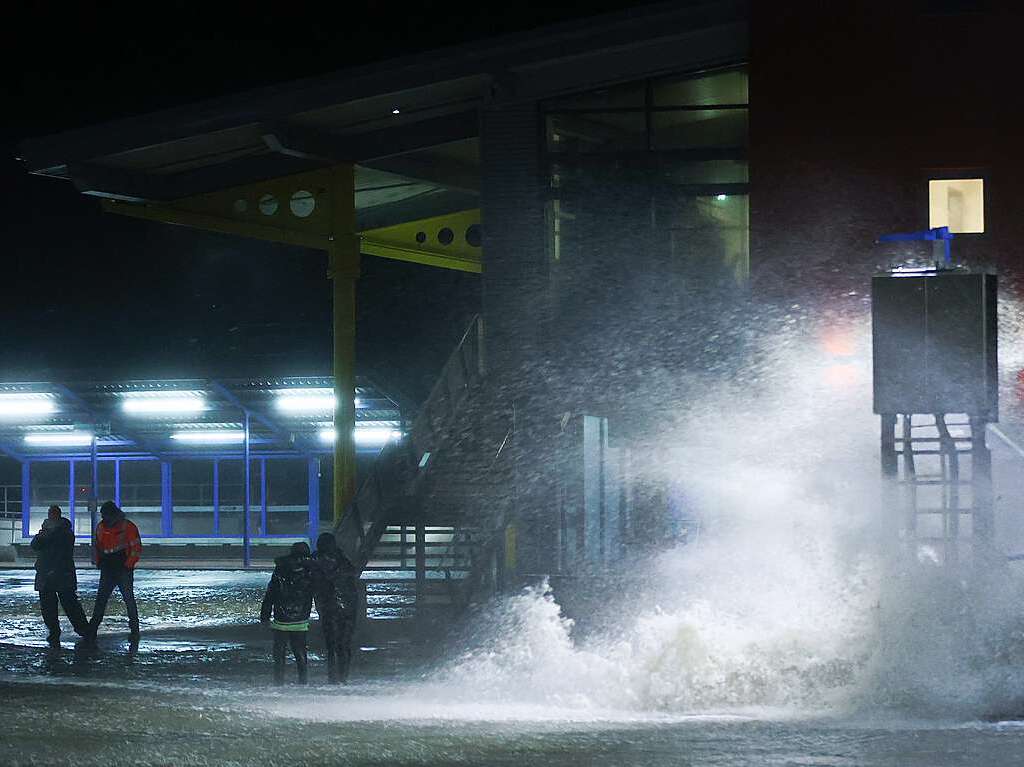 Passanten sind neben der Gischt der aufgepeitschten Nordsee am berfluteten Fhranleger Dagebll unterwegs.